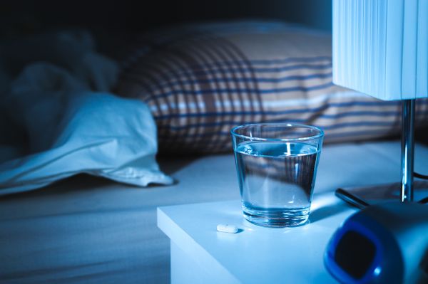 Beside photo of a glass of water and a pill sitting on nigh stand 